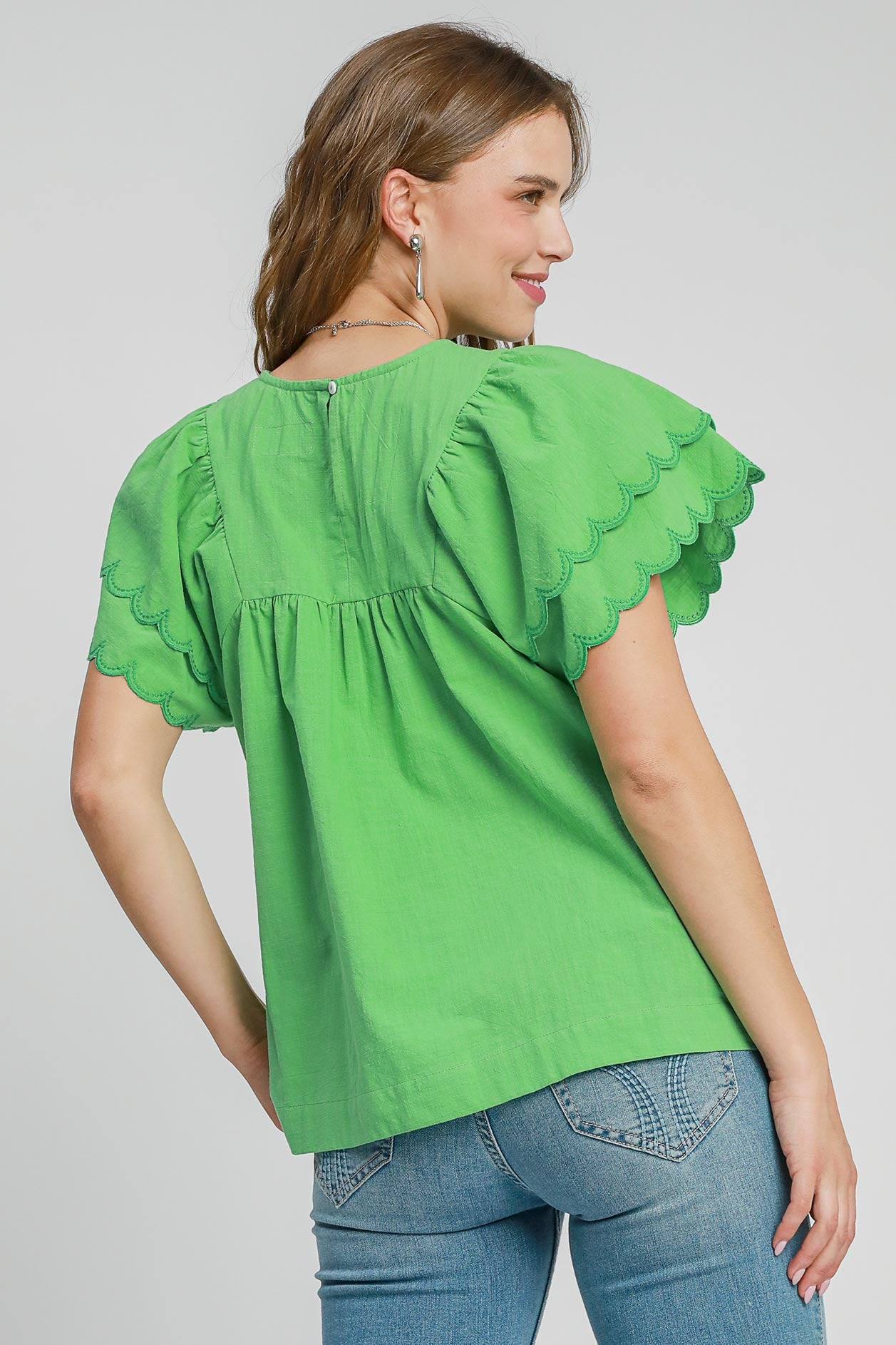 Woman wearing a green blouse with ruffled sleeves on a gray background