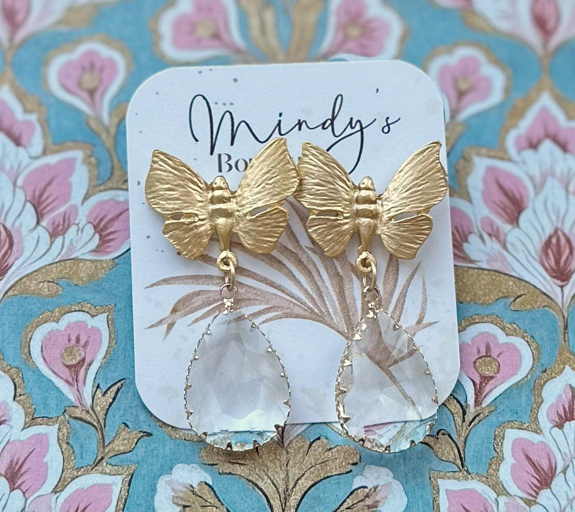 Gold butterfly earrings on a decorative card with floral background