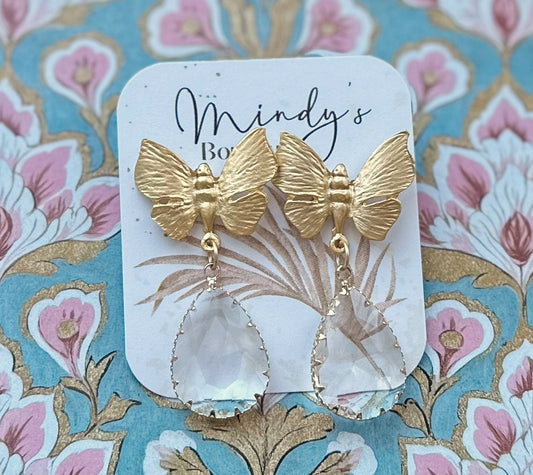 Gold butterfly earrings on a decorative card with floral background