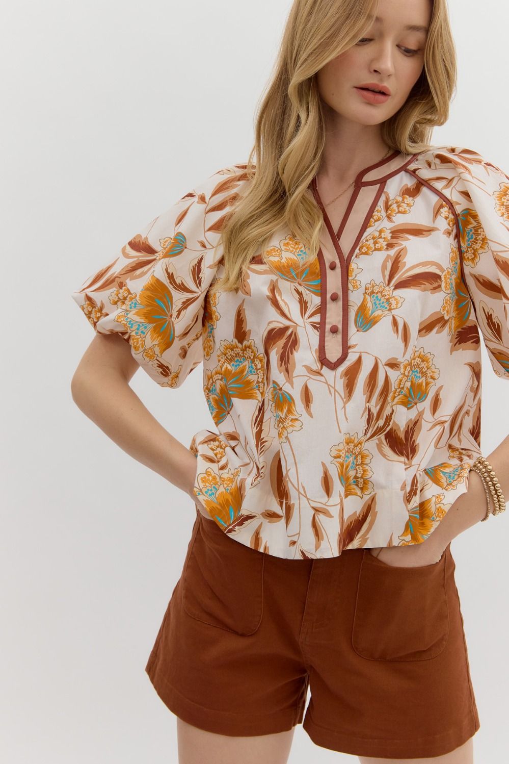 Woman wearing a floral blouse and brown shorts on a white background
