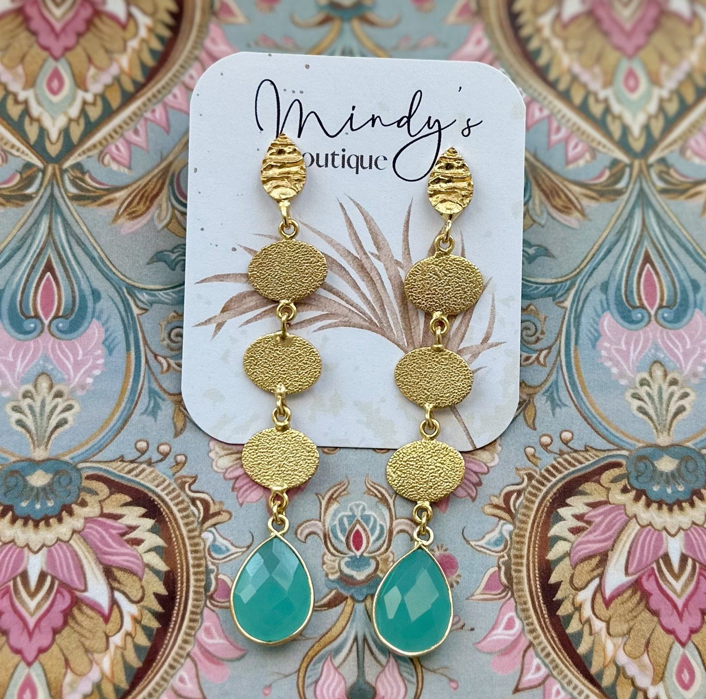 Gold and turquoise earrings on a 'Mindy's Boutique' card with a decorative background