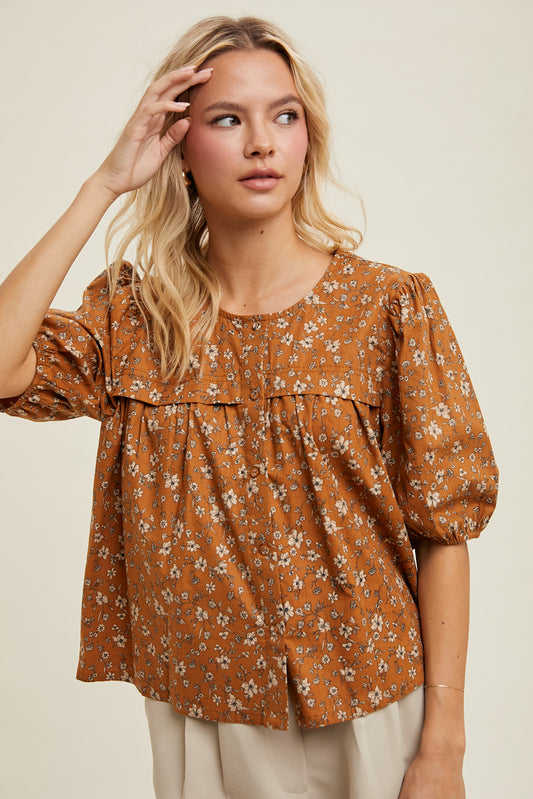 Woman wearing a floral blouse with puff sleeves against a beige background