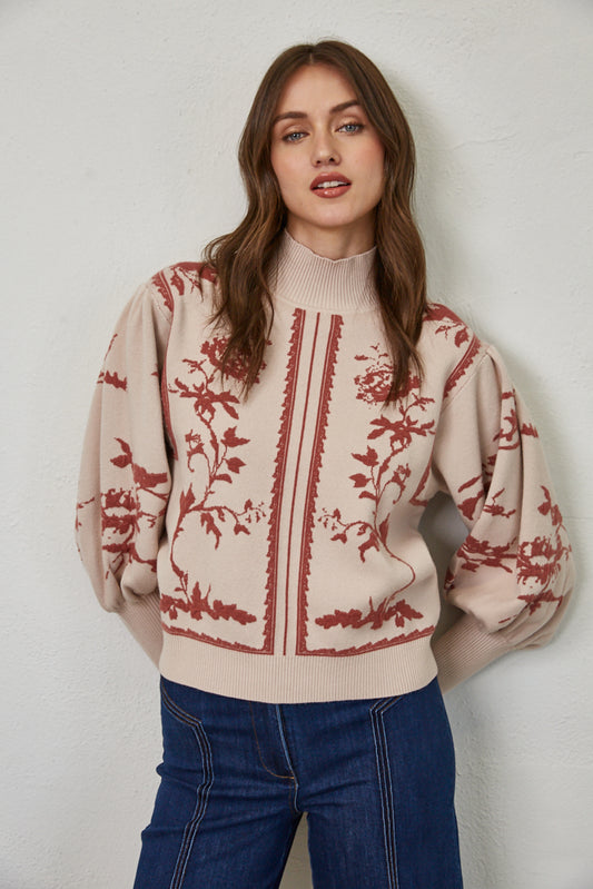 Woman wearing a beige sweater with red floral patterns against a plain background
