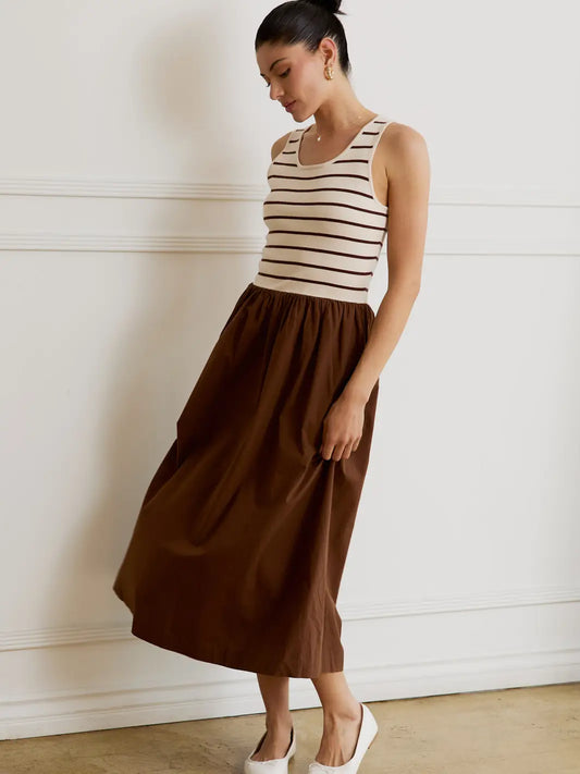 Woman wearing a striped tank top and brown skirt against a white wall.