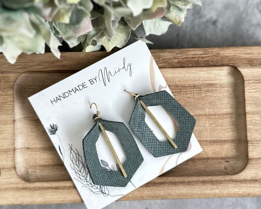 The Marion Earrings are perfect for fall with a soft gray hexagon leather puckered with a gold bar accent. They are so unique and will make a statement with any outfit.

Hypoallergenic, lightweight, nickel, lead, and cadmium free.

Length 2.5 inches