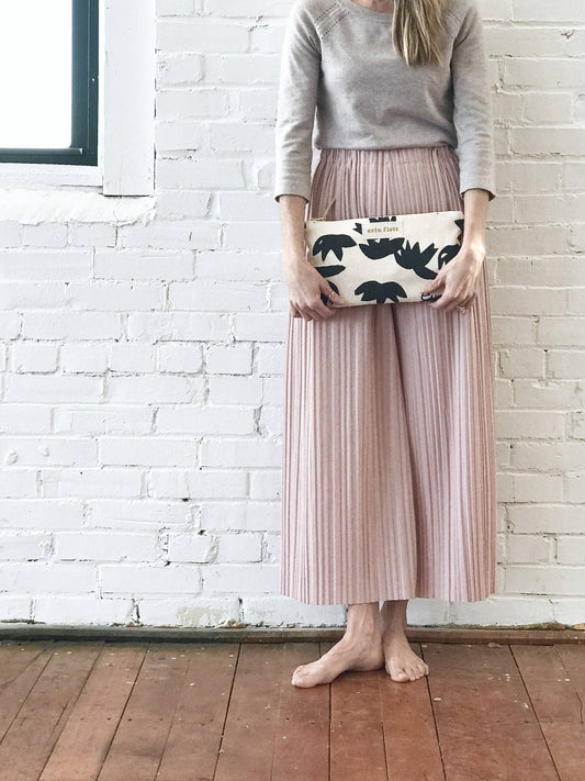 Person holding a floral clutch against a white brick wall.