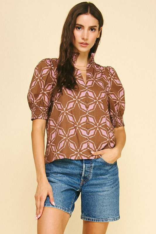 Woman wearing a patterned top and denim shorts on a beige background